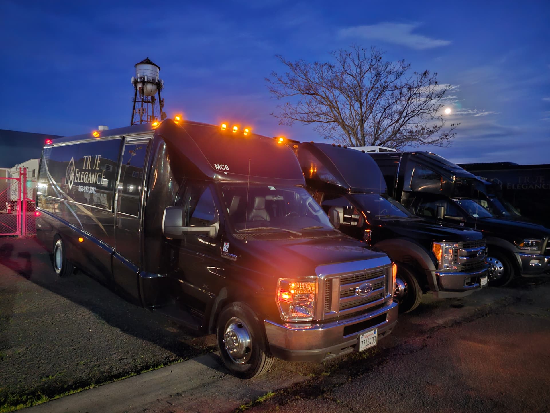 Mini coach fleet at dusk Three black True Elegance mini coach buses parked in a lot at dusk with running lights on
