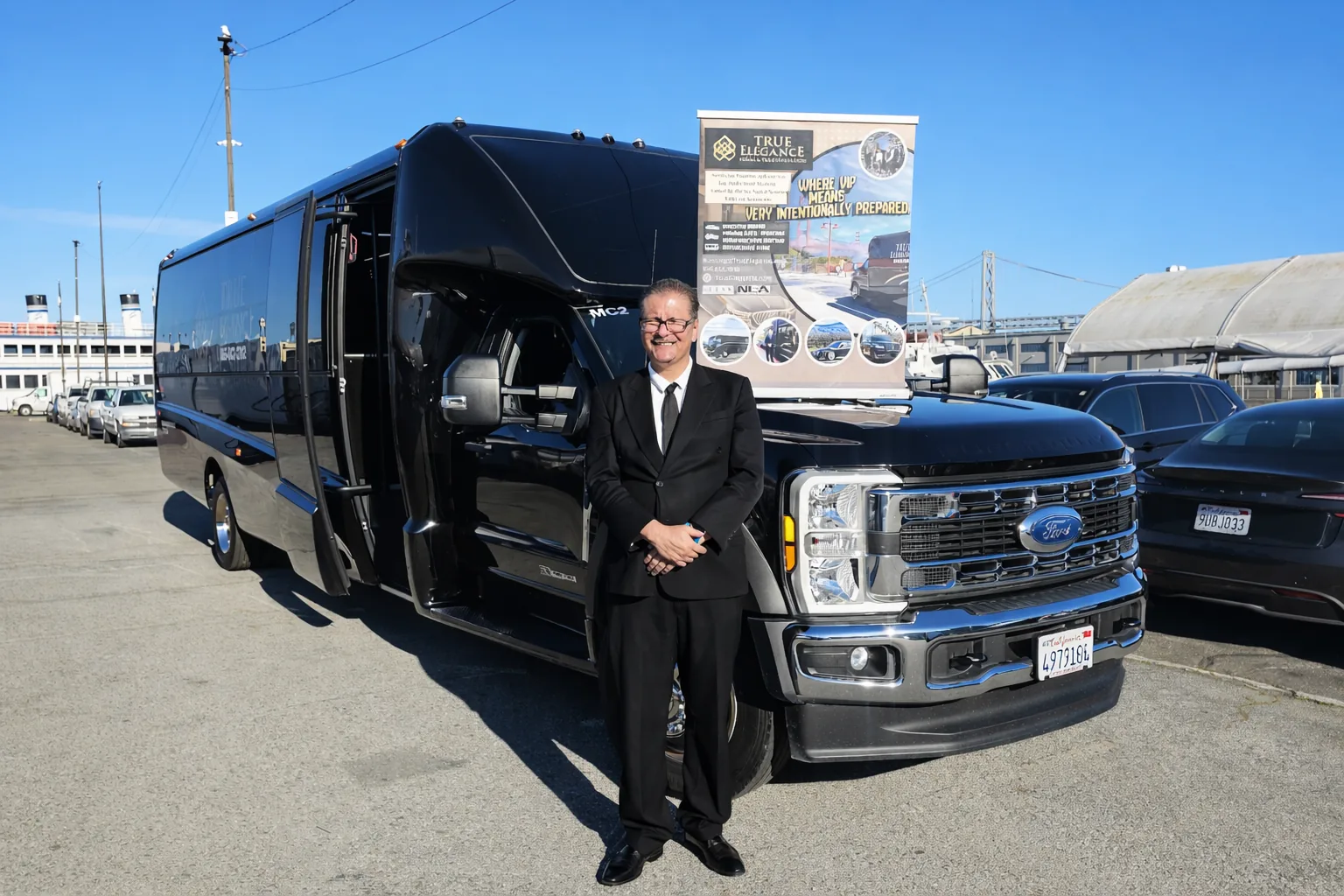 True Elegance chauffeur in a black suit standing beside a black Grech executive shuttle bus